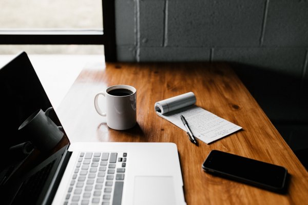 calculator, laptop and phone on a desk beside a mug of coffee